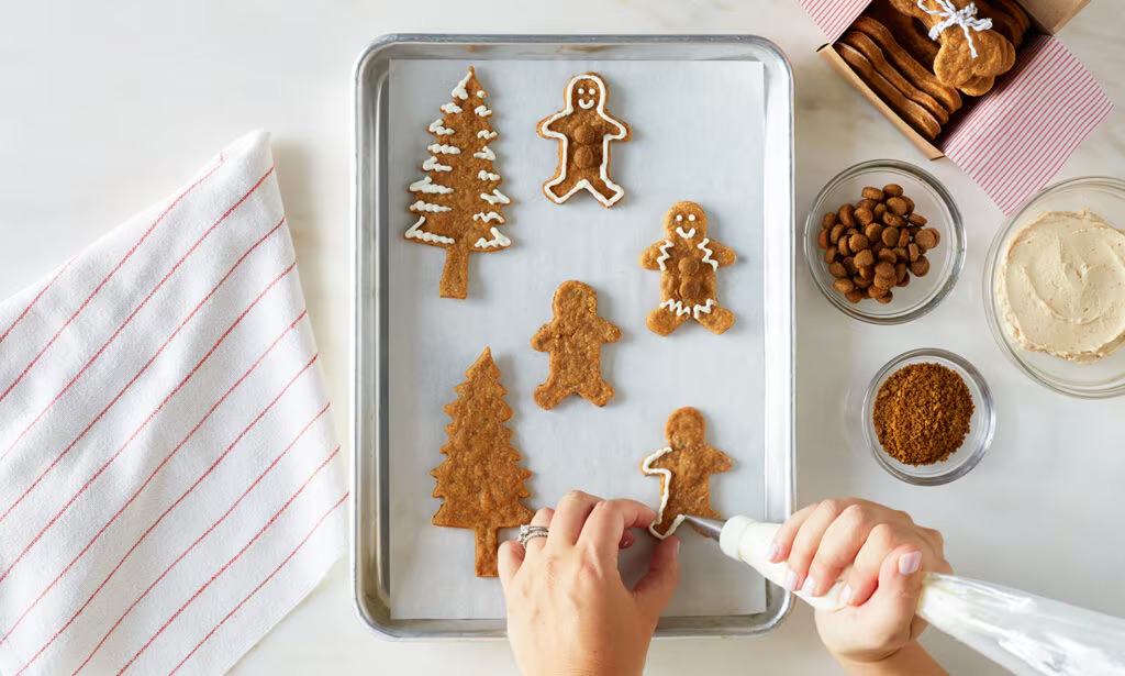 Photo of a hands piping a design onto dog treats in the shapes of gingerbread men and Christmas trees